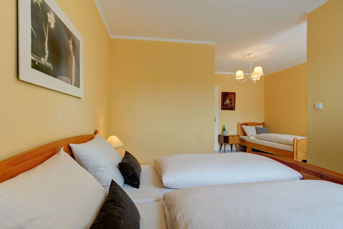 A hotel room with two beds, a nightstand, a lamp, a painting on the wall, and a small table with a chair.