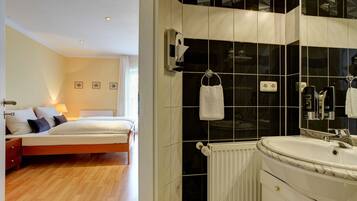 A hotel room with a bed, bedside table, and a bathroom with a sink and mirror.