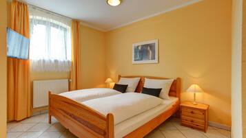 Un dormitorio con cama de madera, dos mesitas de noche, televisor en la pared y ventana con cortinas.