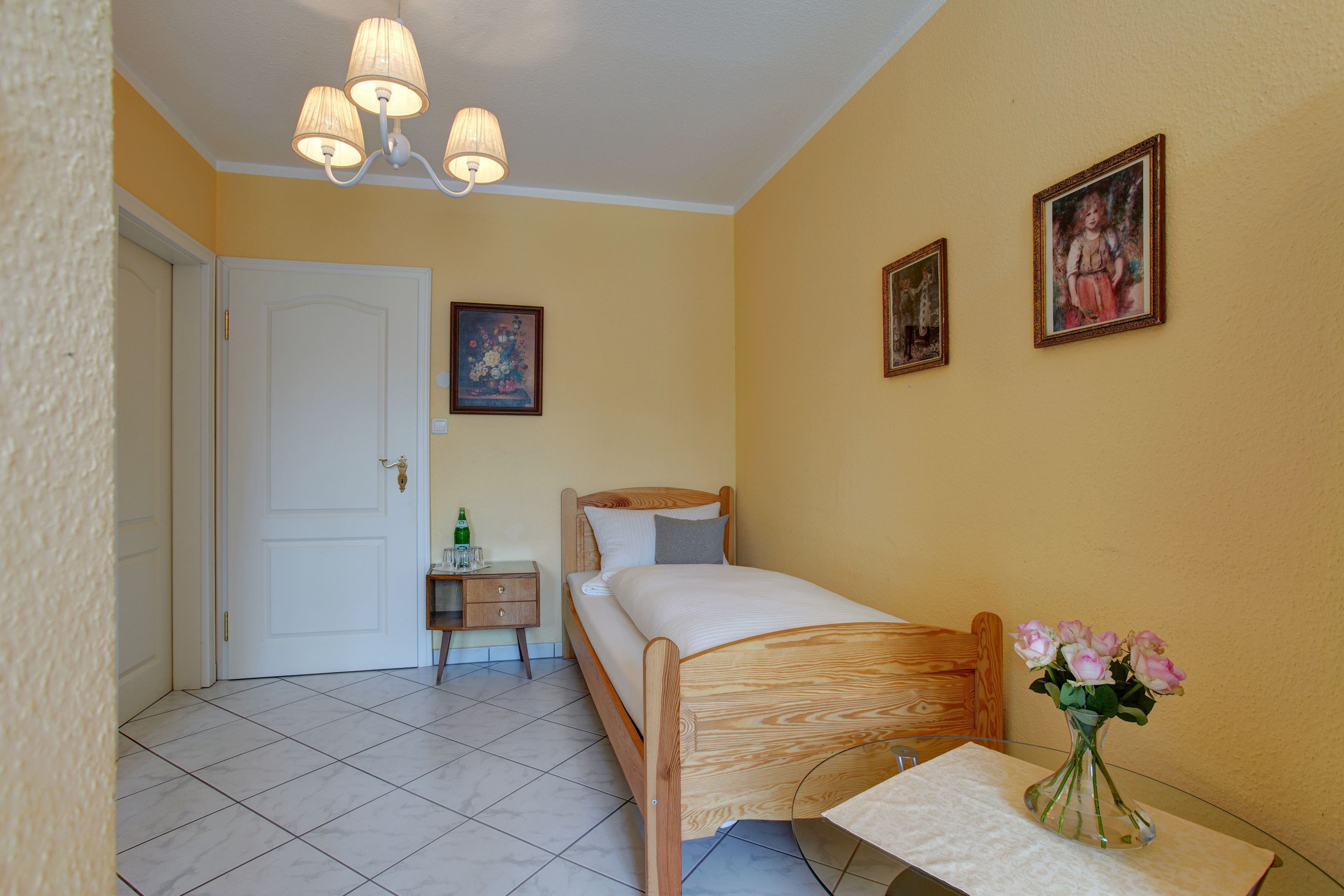 Quarto com cama, mesa de cabeceira, abajur e um vaso com flores.