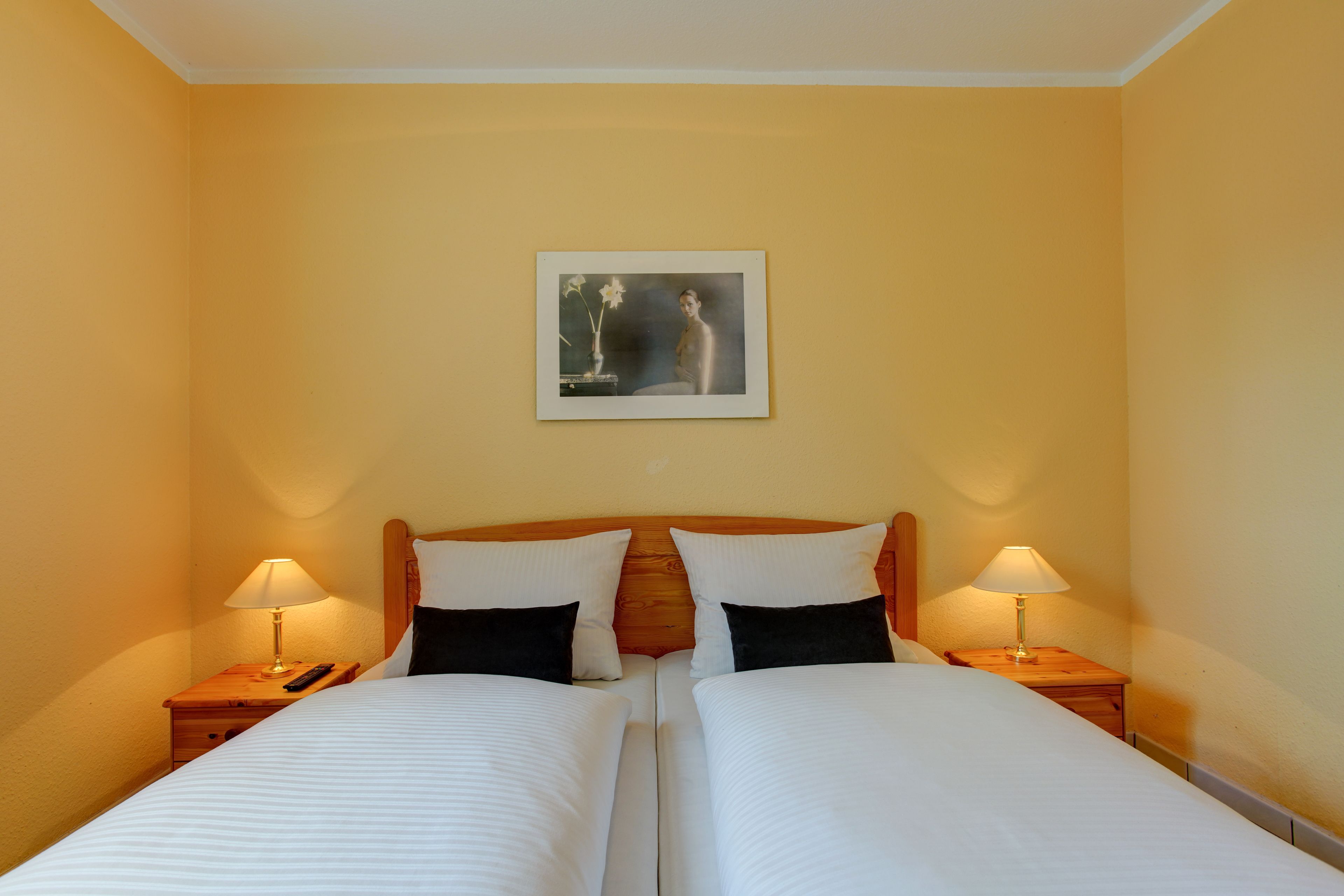 A double bed with white linens, two bedside tables with lamps, and a framed artwork on the wall.