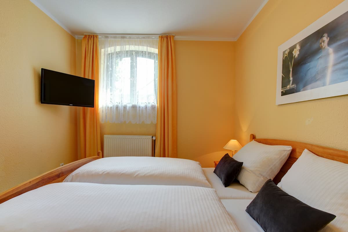 A hotel room with two beds, a TV, a painting, and a window with curtains.