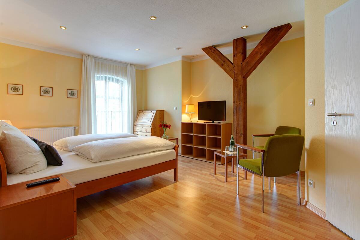 A bedroom with a bed, a desk, a chair, a TV, and a wooden beam structure.