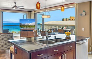 A kitchen with a large island, a dining area with chairs and a table, and a view of the ocean.