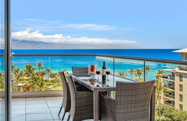 A balcony with wicker furniture, a glass table, and a bottle of wine.