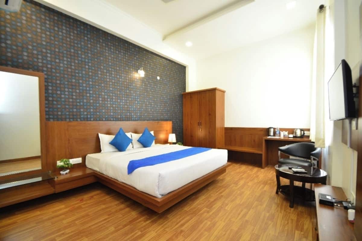 A hotel room with a large bed, wooden headboard, a TV, a desk, and a wardrobe.