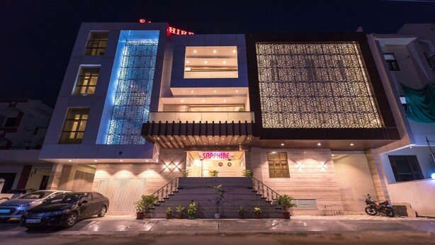 Un hotel moderno con un llamativo letrero 'Sapphire', una escalera que conduce a la entrada y un aparcamiento con coches y motocicletas.