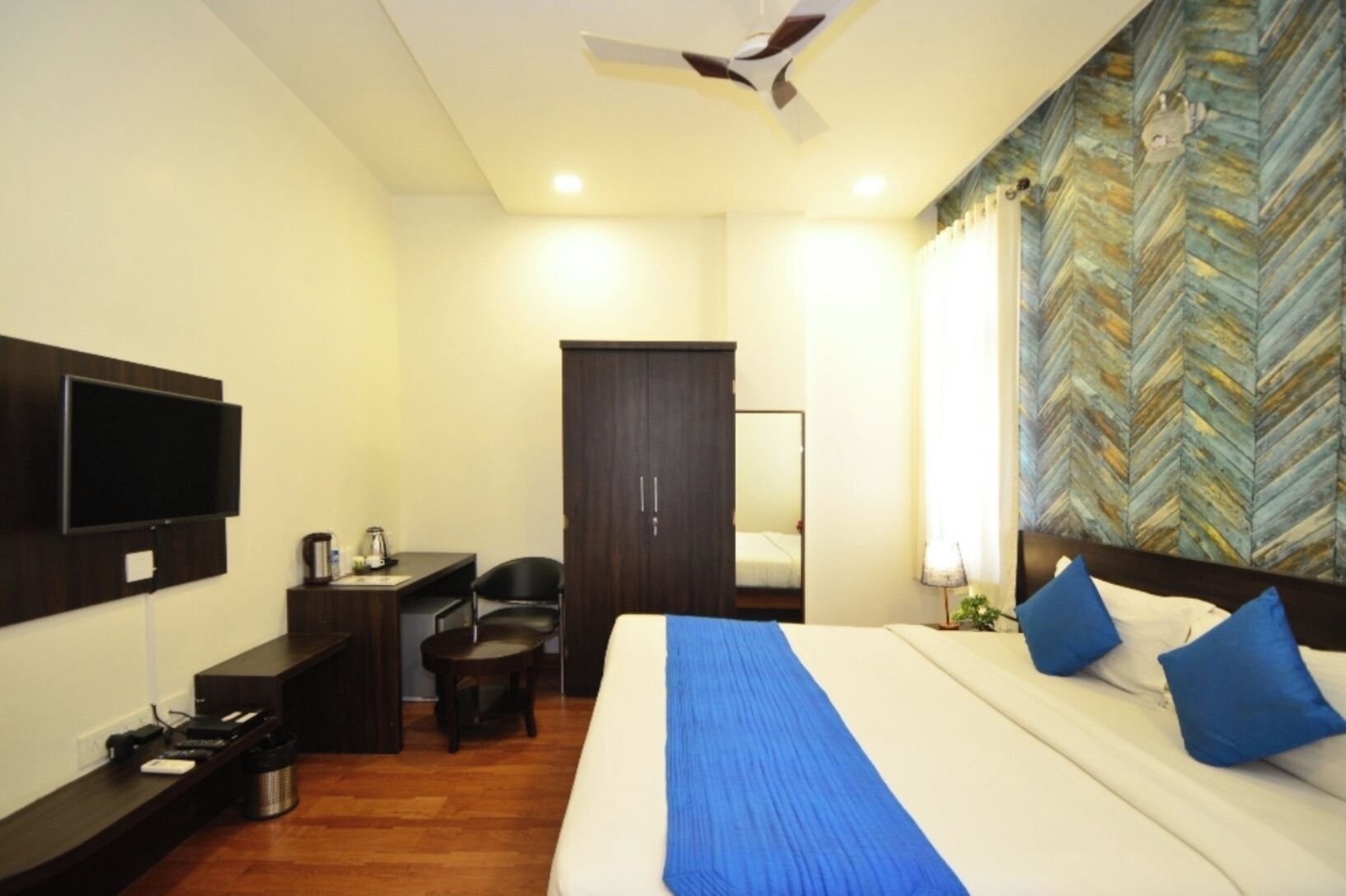 A hotel room with a bed, a desk, a chair, a television, and a ceiling fan.