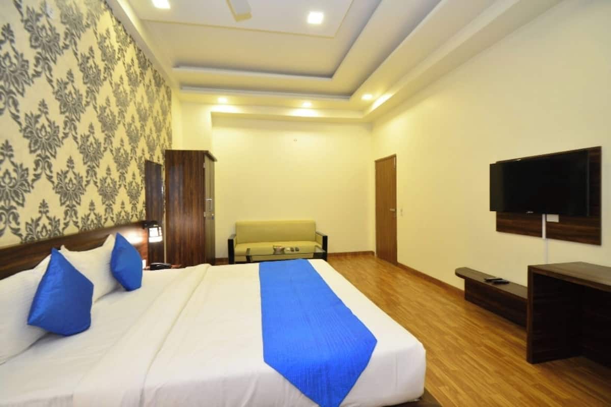 A hotel room with a large bed, a sofa, a television, and a wooden floor.