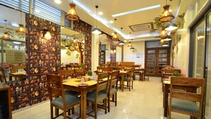 Un restaurante con mesas y sillas de madera, lámparas colgantes y una pared decorativa con diversas imágenes.