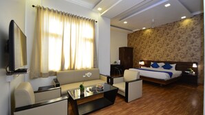 Habitación de hotel con sofá, sillones, una mesa de centro, cama con almohadas azules, mesita de noche y televisor.