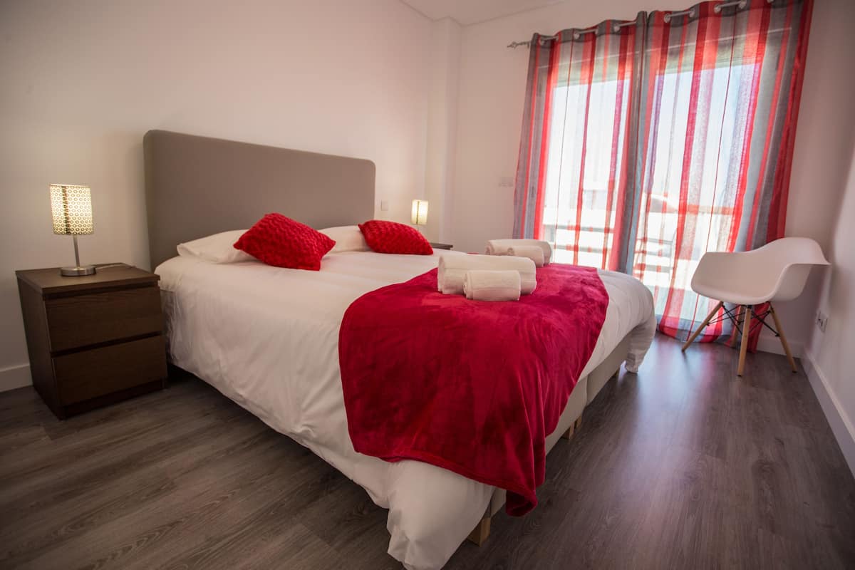 A modern bedroom with a large bed, two bedside tables, a chair, and a window with curtains.