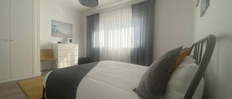 Een slaapkamer met een bed, een kledingkast, een bureau en een raam met gordijnen.
