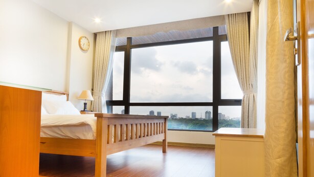 A hotel room with a bed, bedside table, lamp, and a large window with curtains. - Lake House Studio (Hanoi)
