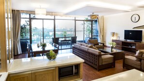 A modern living room with a sofa set, a dining table with a bowl of fruit, a TV, and a balcony with a view of the city. - Lake House Studio (Hanoi)