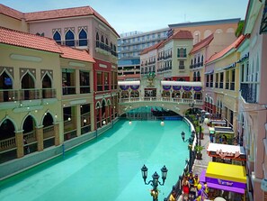 Une vaste place intérieure agrémentée d’une fontaine centrale, entourée d’immeubles à plusieurs étages dotés de balcons et de boutiques.