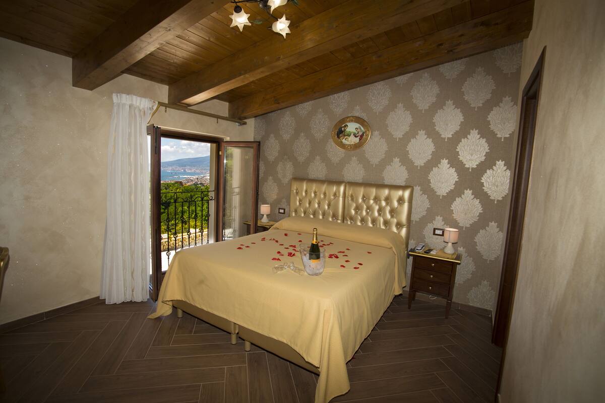Ein Schlafzimmer mit einem großen Bett, einem Nachttisch, einer Lampe und Blick ins Freie.