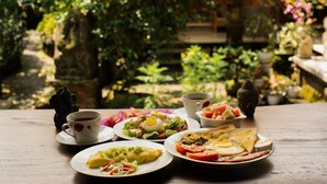 Ett bord dukat med frukostmat, inklusive ägg, rostat bröd och frukt, placerat utomhus med grönska i bakgrunden.