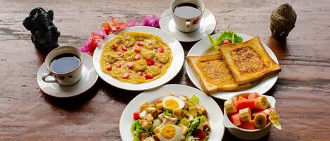 A wooden table with breakfast items including toast, a salad, and a bowl of fruit.