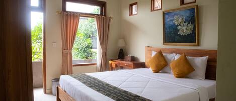 A hotel room with a bed, a desk, a chair, a lamp, and a window with curtains.