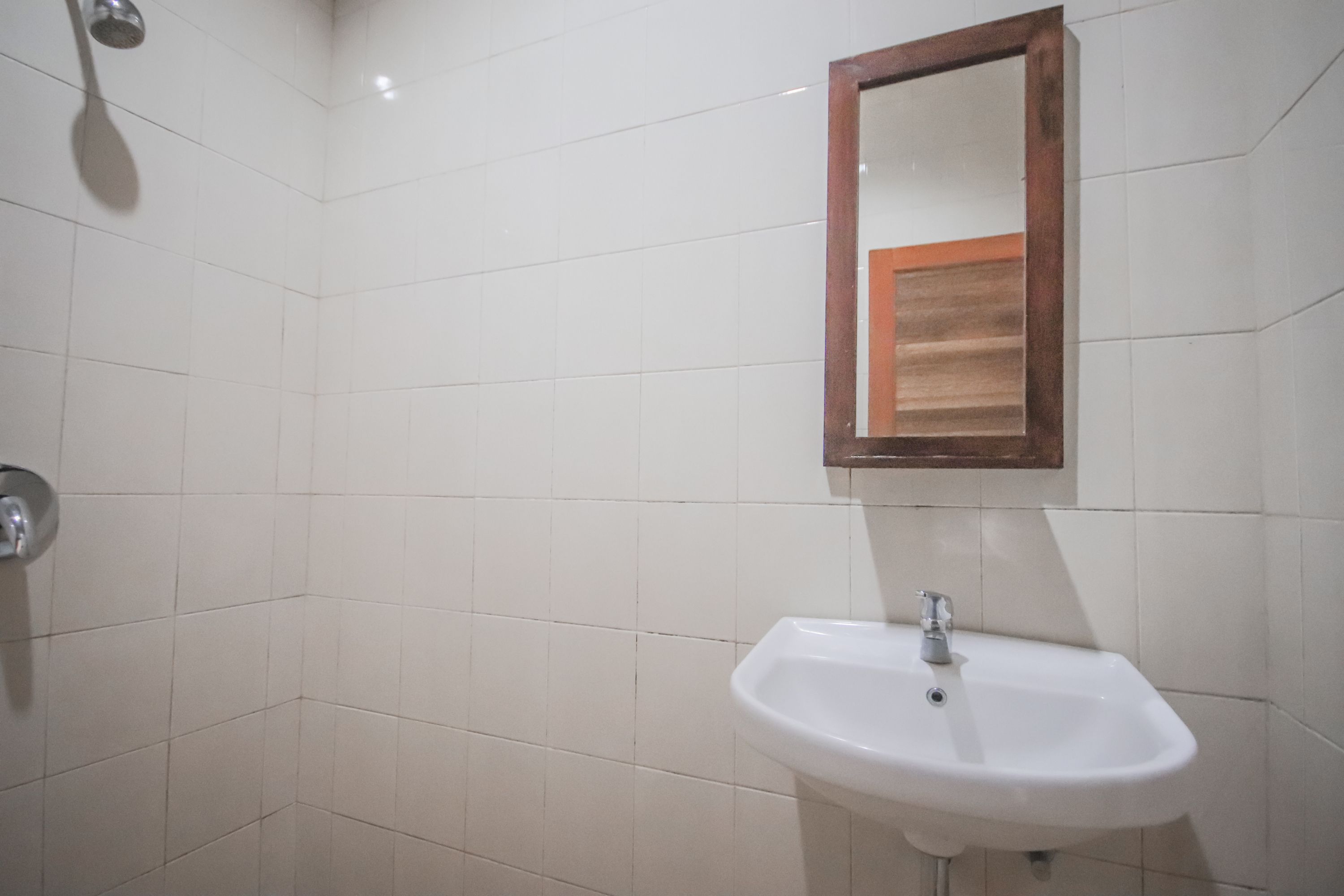 Une salle de bain avec des murs recouverts de carreaux blancs, un lavabo blanc et un miroir à cadre en bois.