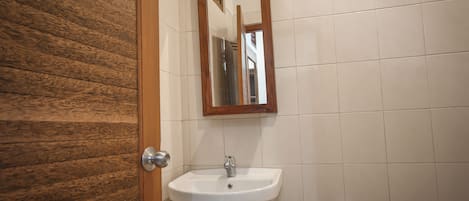 A bathroom with a wooden door, white tiled walls, and a white sink with a mirror above it.
