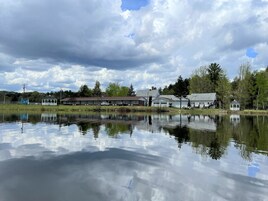 A lakeside property with a gazebo, a building with a red roof, and a small white structure near the water.