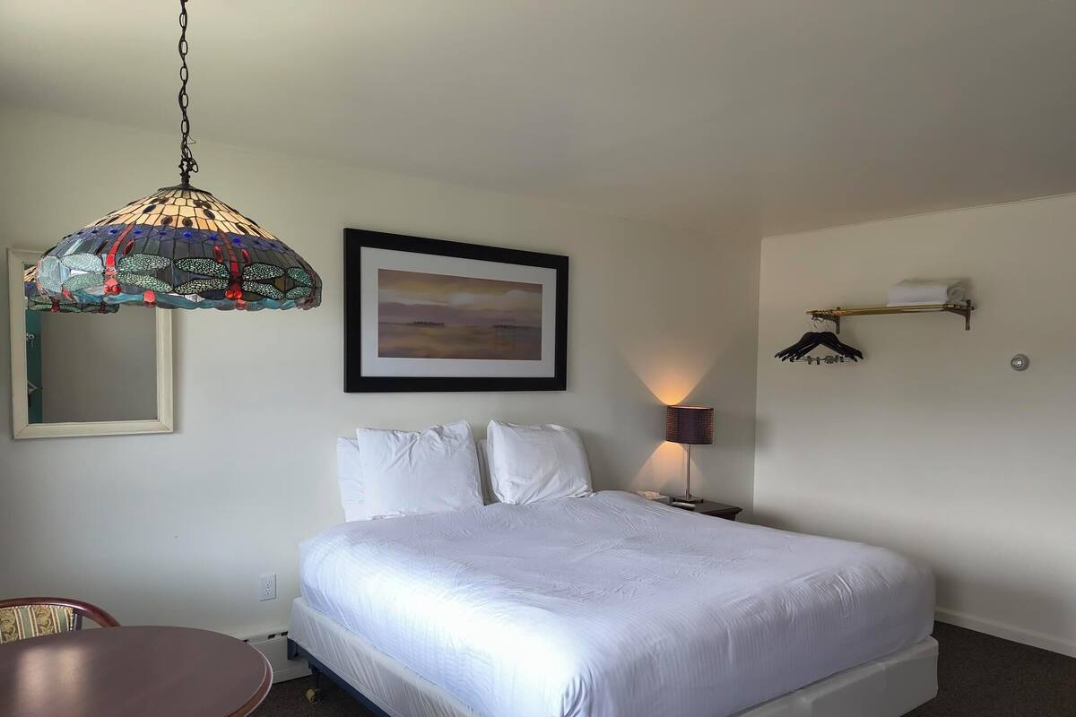 A neatly arranged hotel room with a bed, bedside table, lamp, and a hanging light fixture.