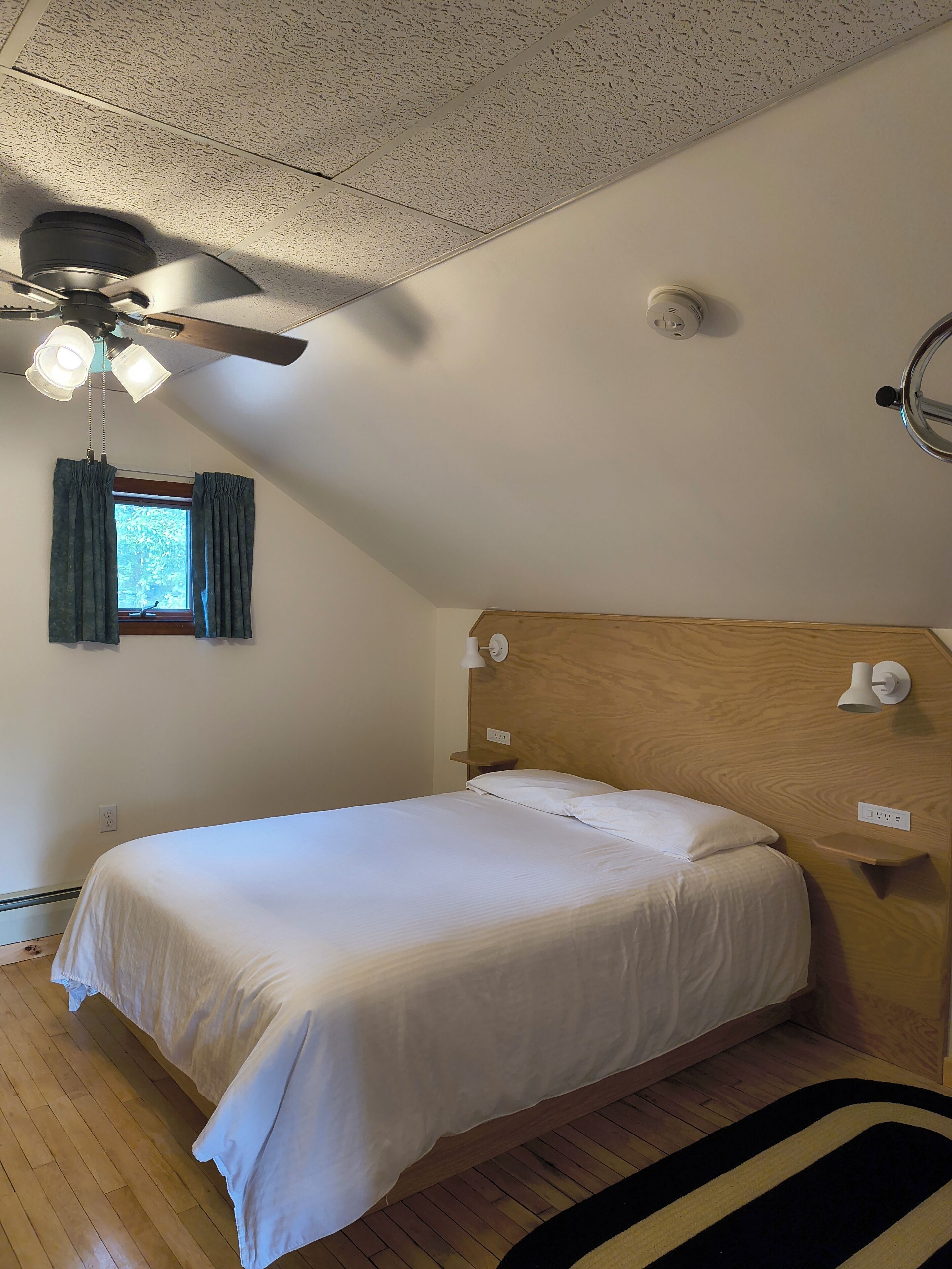 A bedroom with a single bed, a ceiling fan, a window with curtains, and a wooden headboard.