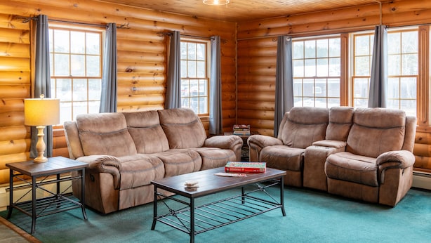 A log cabin interior with a sofa set, a coffee table, and a ceiling fan. - Sara Placid Inn & Suites (Saranac Lake)