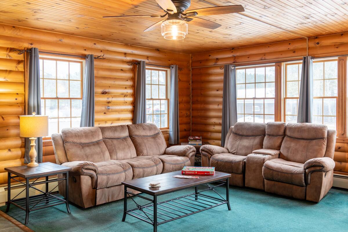 A log cabin interior with a sofa set, a coffee table, and a ceiling fan.