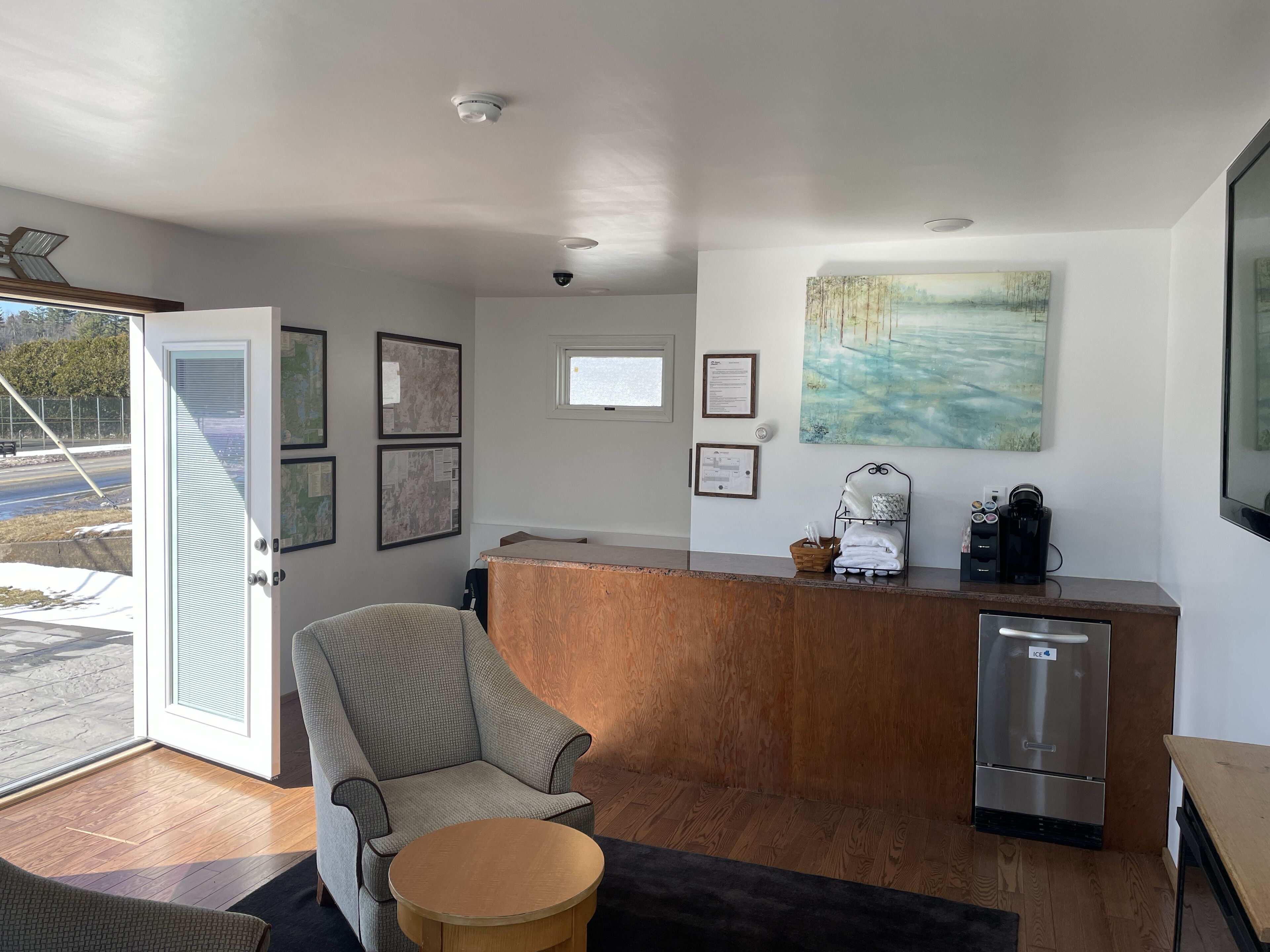 A modern kitchen with a wooden counter, a refrigerator, and a chair. There are framed pictures on the wall and a window above the counter.