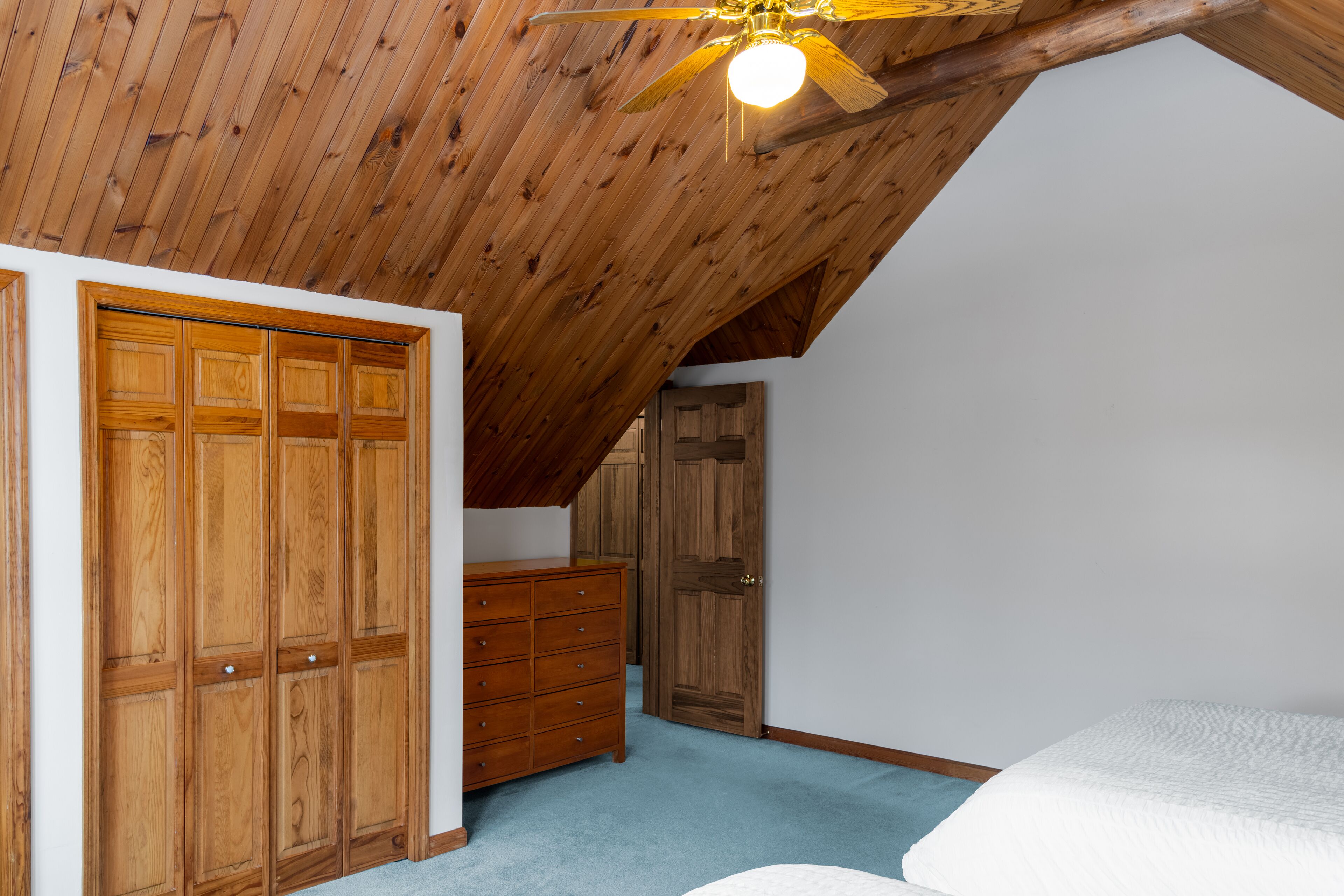 A bedroom with a sloped ceiling, wooden wardrobe, and a bed.