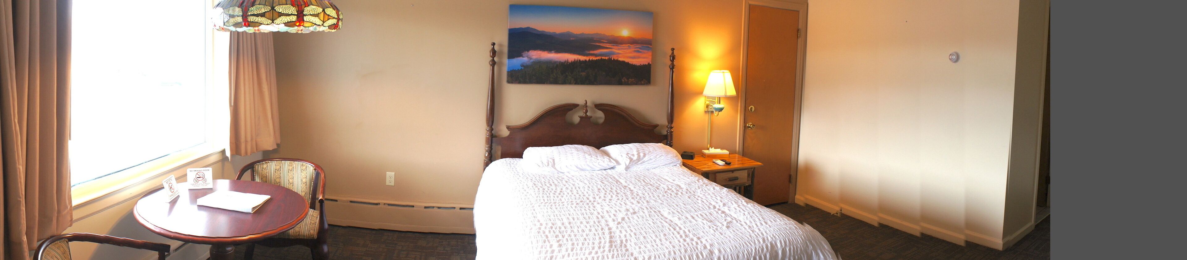 Een hotelkamer met een bed, een stoel, een klein tafeltje, een lamp en een schilderij aan de muur.