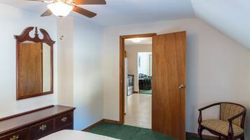 A bedroom with a bed, dresser, chair, wooden door, and a ceiling fan.