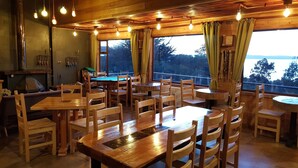 Um restaurante acolhedor com mobiliário de madeira e grandes janelas que oferecem vista para o exterior.