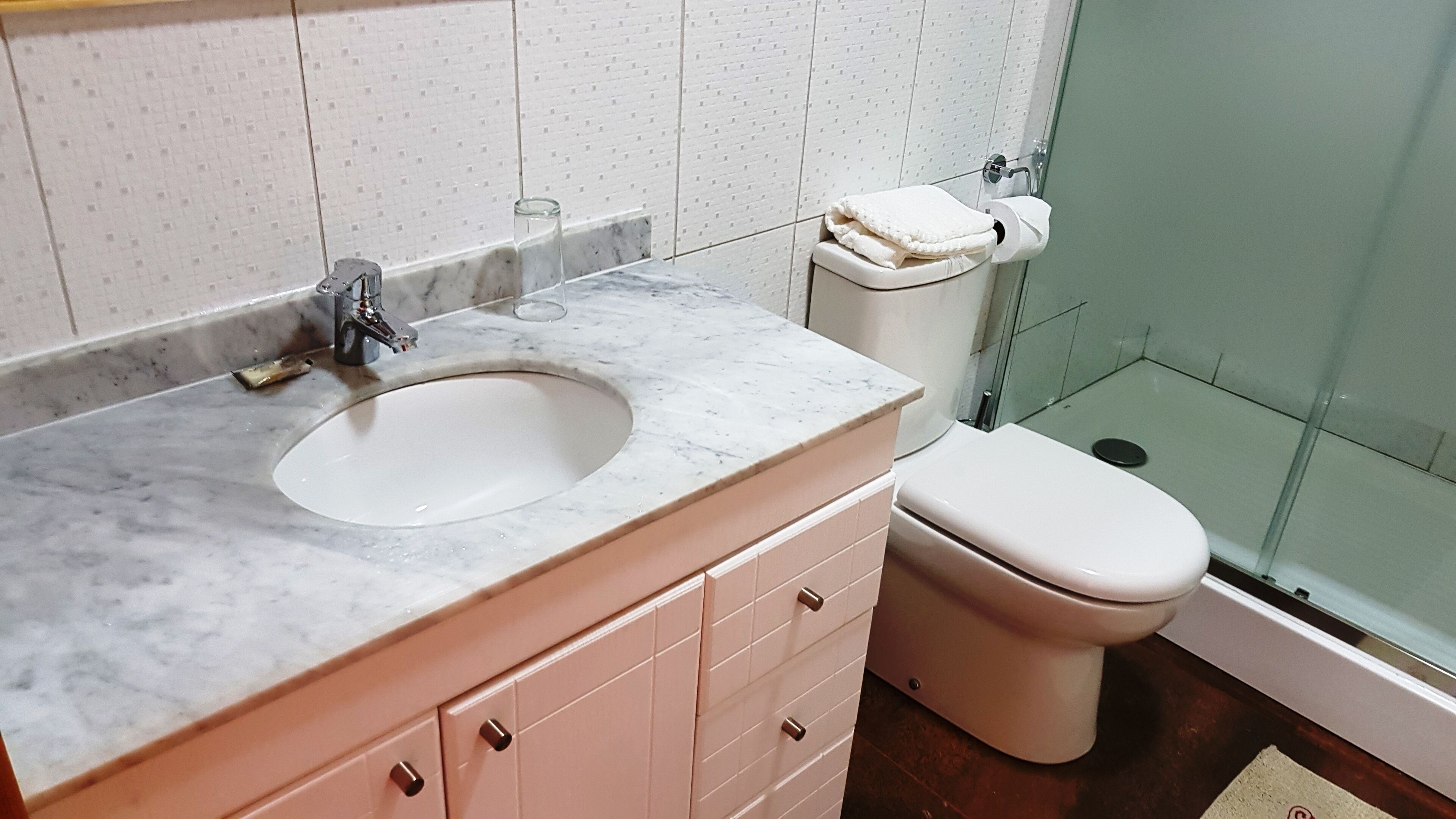 Baño con lavamanos de mármol, inodoro y cabina de ducha de vidrio.
