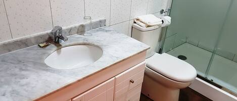 Baño con lavamanos de mármol, inodoro y cabina de ducha de vidrio.