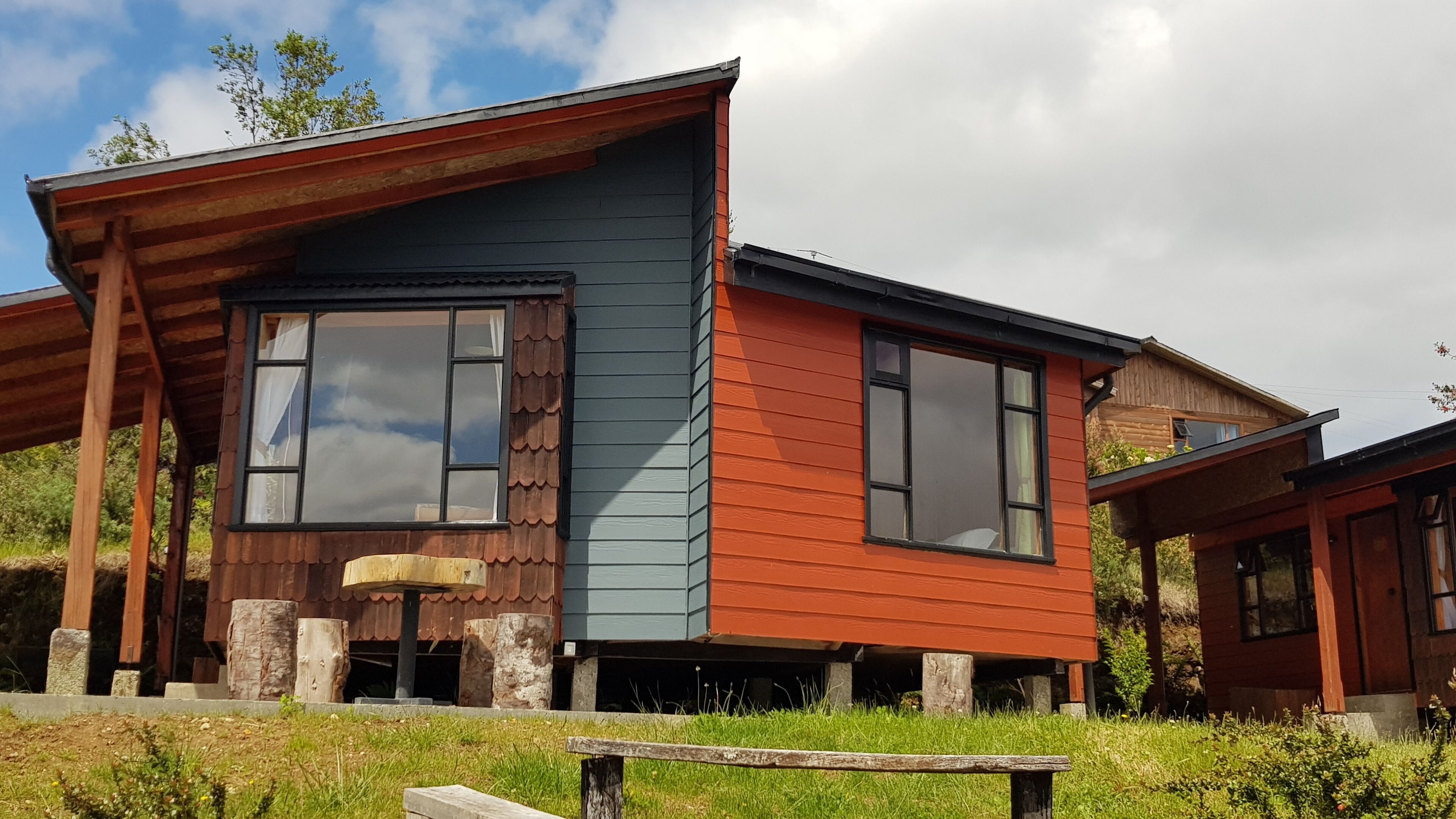 Una casa moderna con un amplio ventanal, un porche de madera y un banco de piedra.