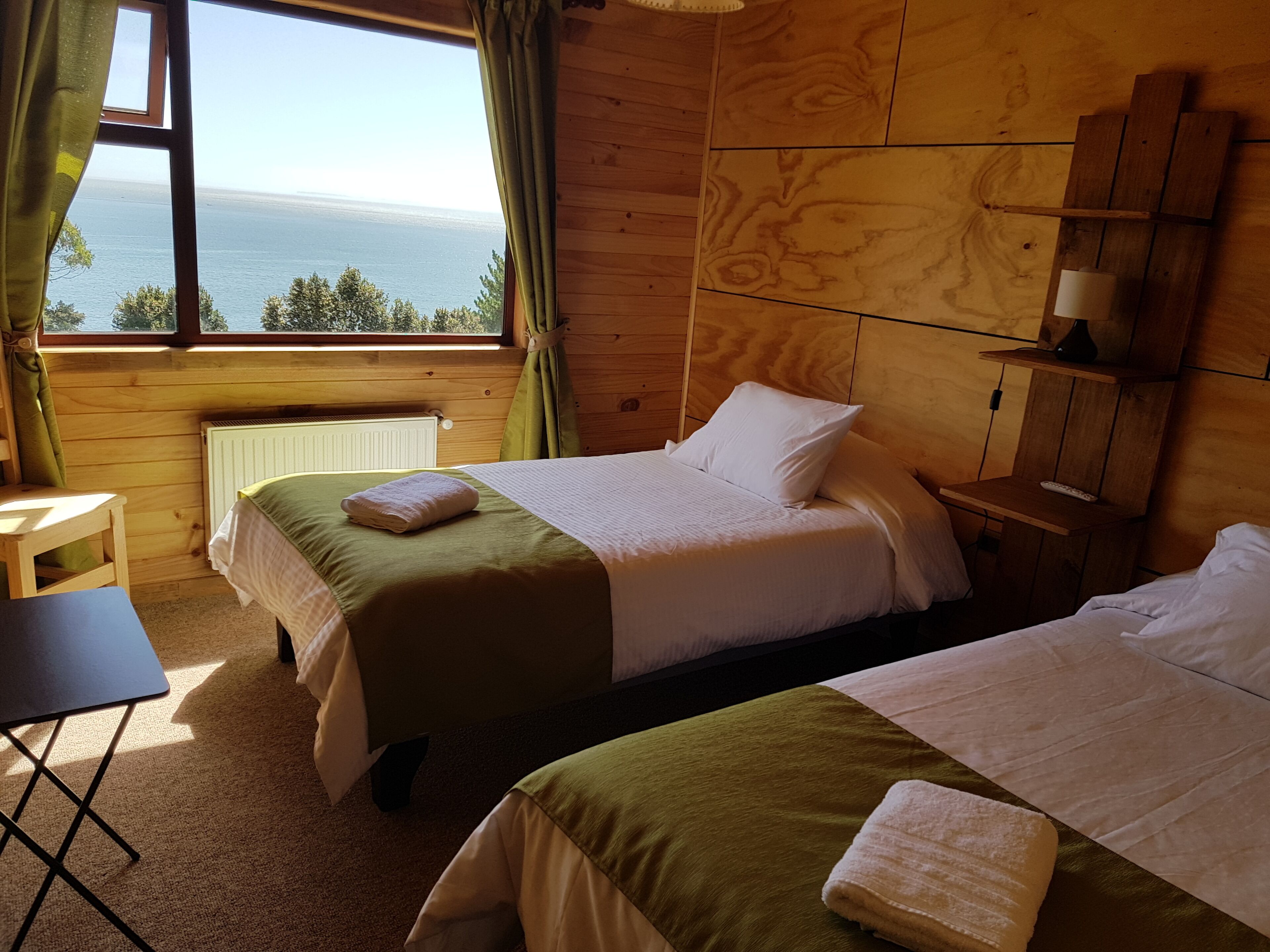 Une chambre avec deux lits, une petite table, une chaise et une vue sur la mer.