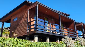 Een houten chalet met balkon, omgeven door groen.