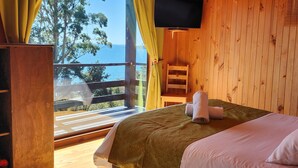 Quarto de cabana de madeira com uma cama, uma TV e uma varanda com vista para o mar.