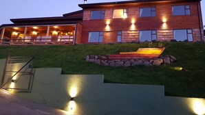 Uma casa de madeira de dois andares com telhado inclinado, uma parede de suporte de pedra e um pequeno jardim com um vaso colorido.