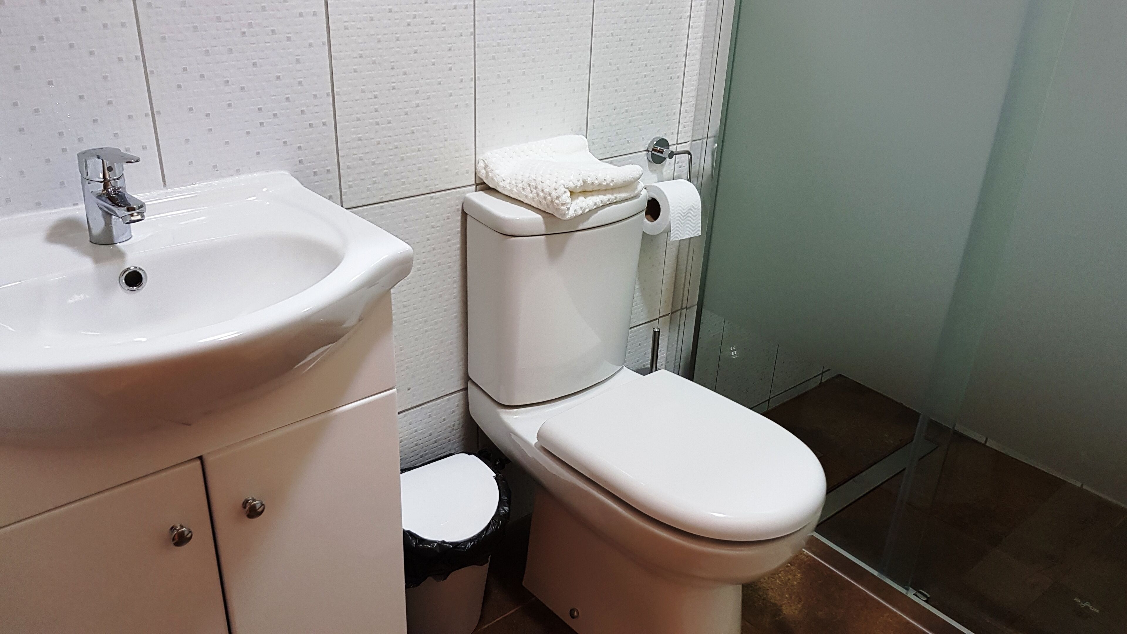 Un baño con lavamanos blanco, inodoro y cubo de basura.