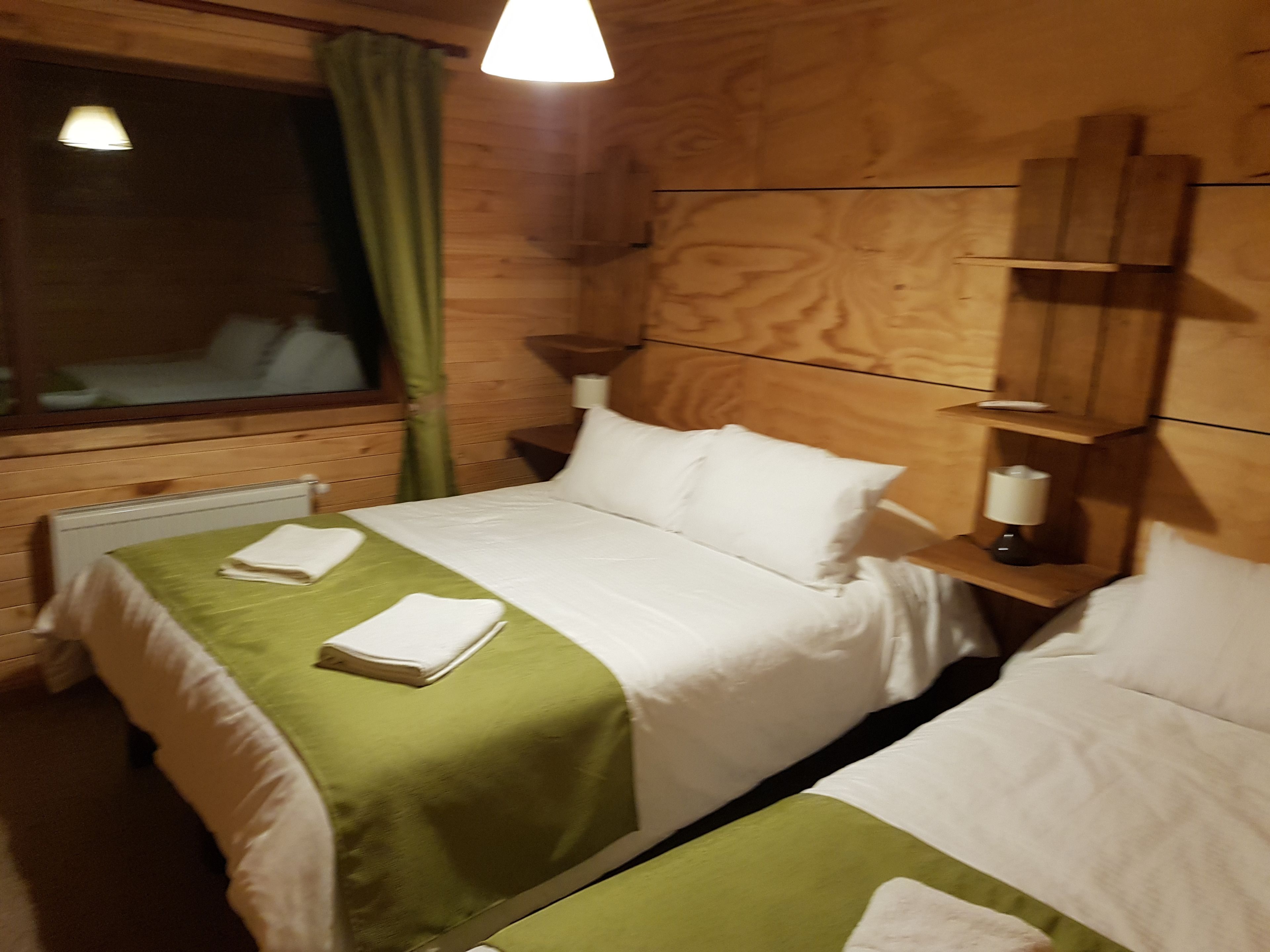 A wooden room with a bed, a nightstand, and a window with curtains.