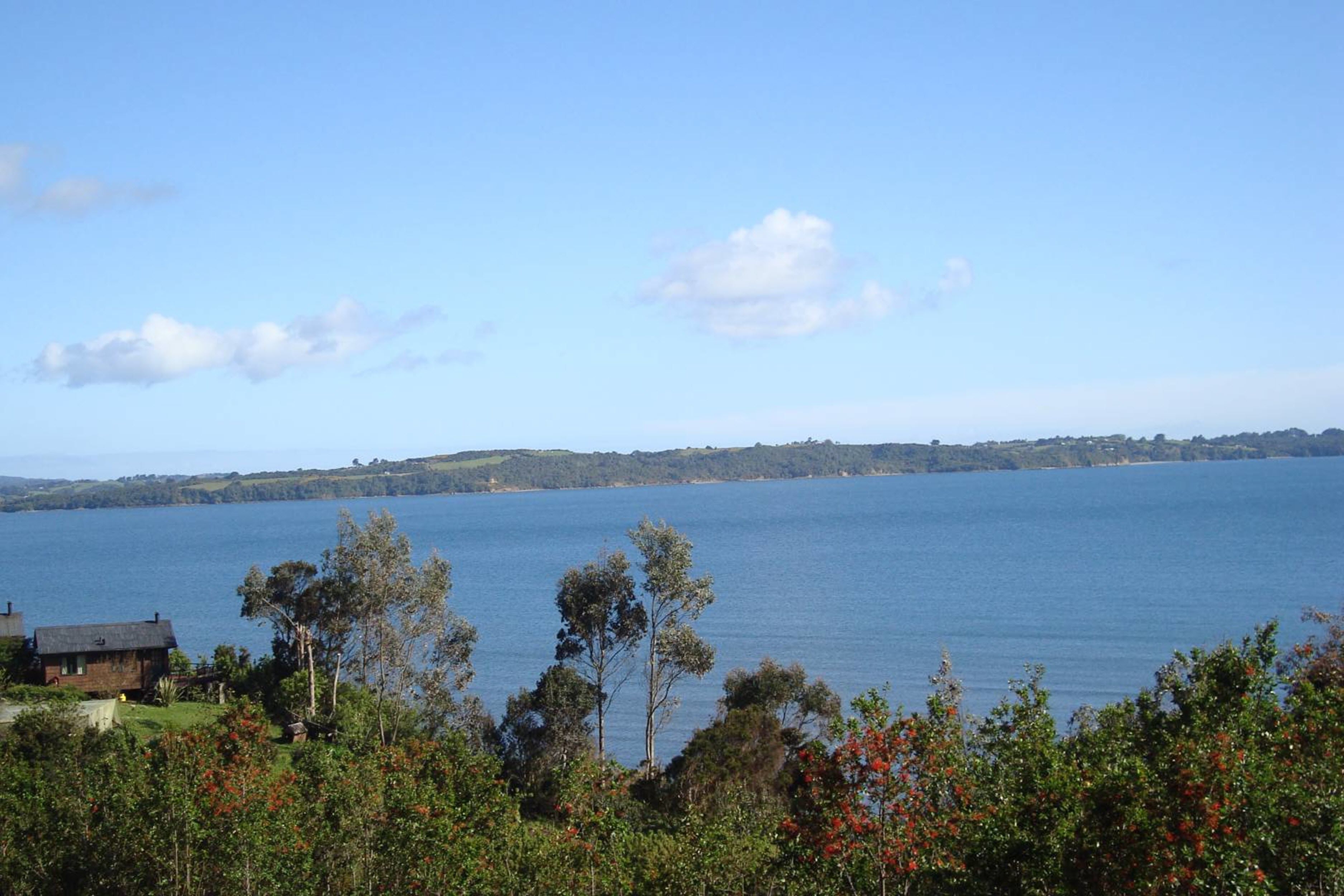 Un lago con una casa en primer plano y una orilla lejana.