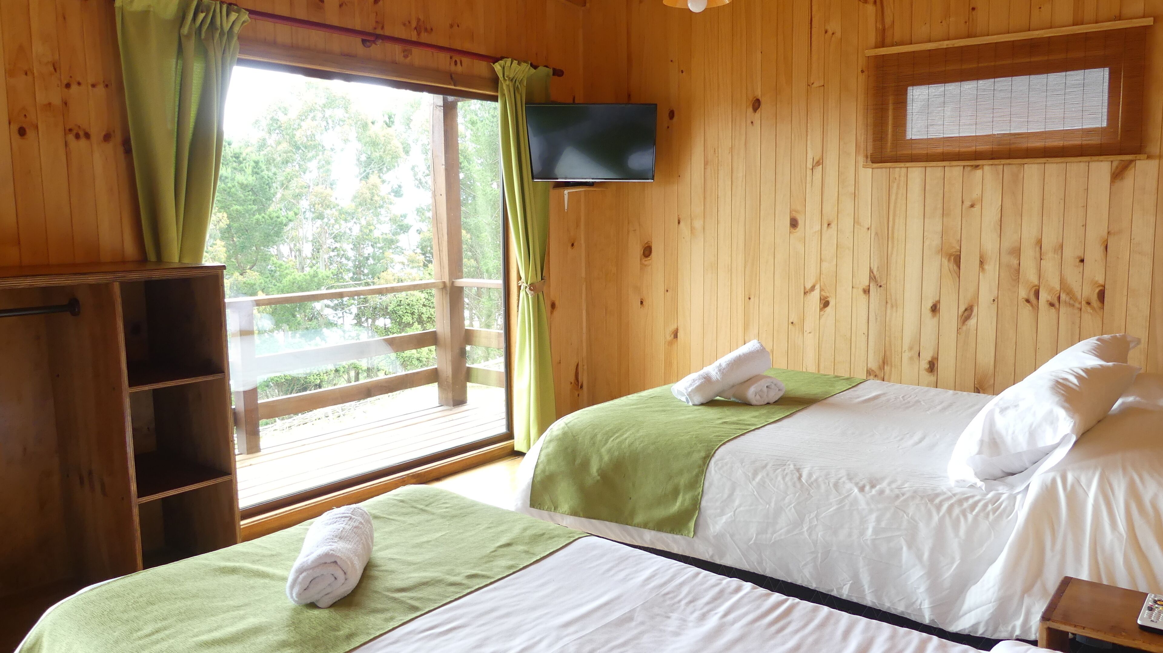 A wooden room with two beds, a TV on the wall, and a window with curtains.