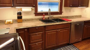 A kitchen with wooden cabinets, a stainless steel sink, a dishwashing machine, and a window with a view of the outdoors. - "Driftwood Island Retreat" Spectacular View, Private Waterfront on James Point. (Vashon)