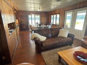 A cozy room with a brown leather sofa, a wooden dining table, and a view through a glass door.