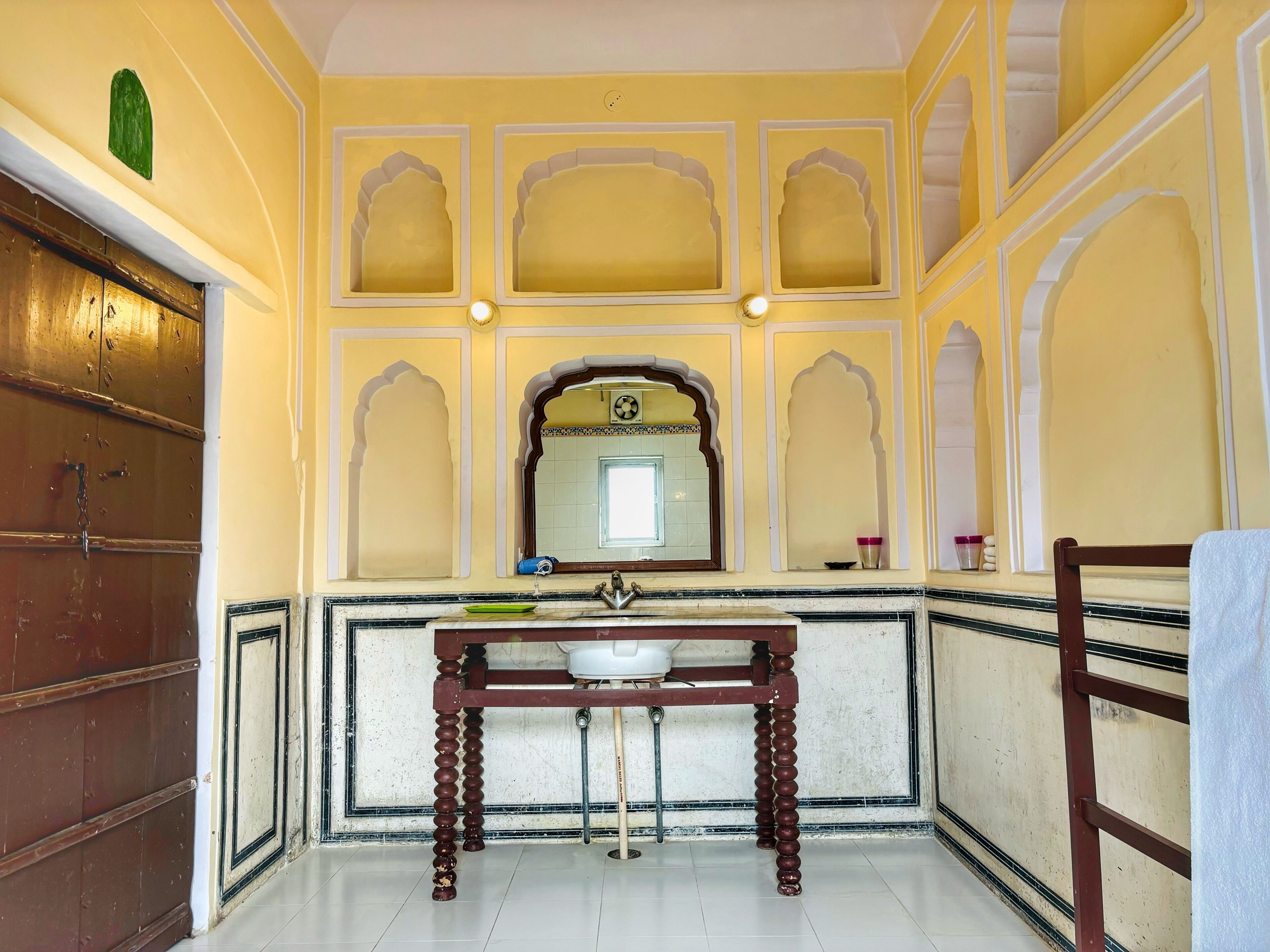 Una habitación tradicional con puerta de madera, lavamanos de mármol y espejo con marco decorativo.